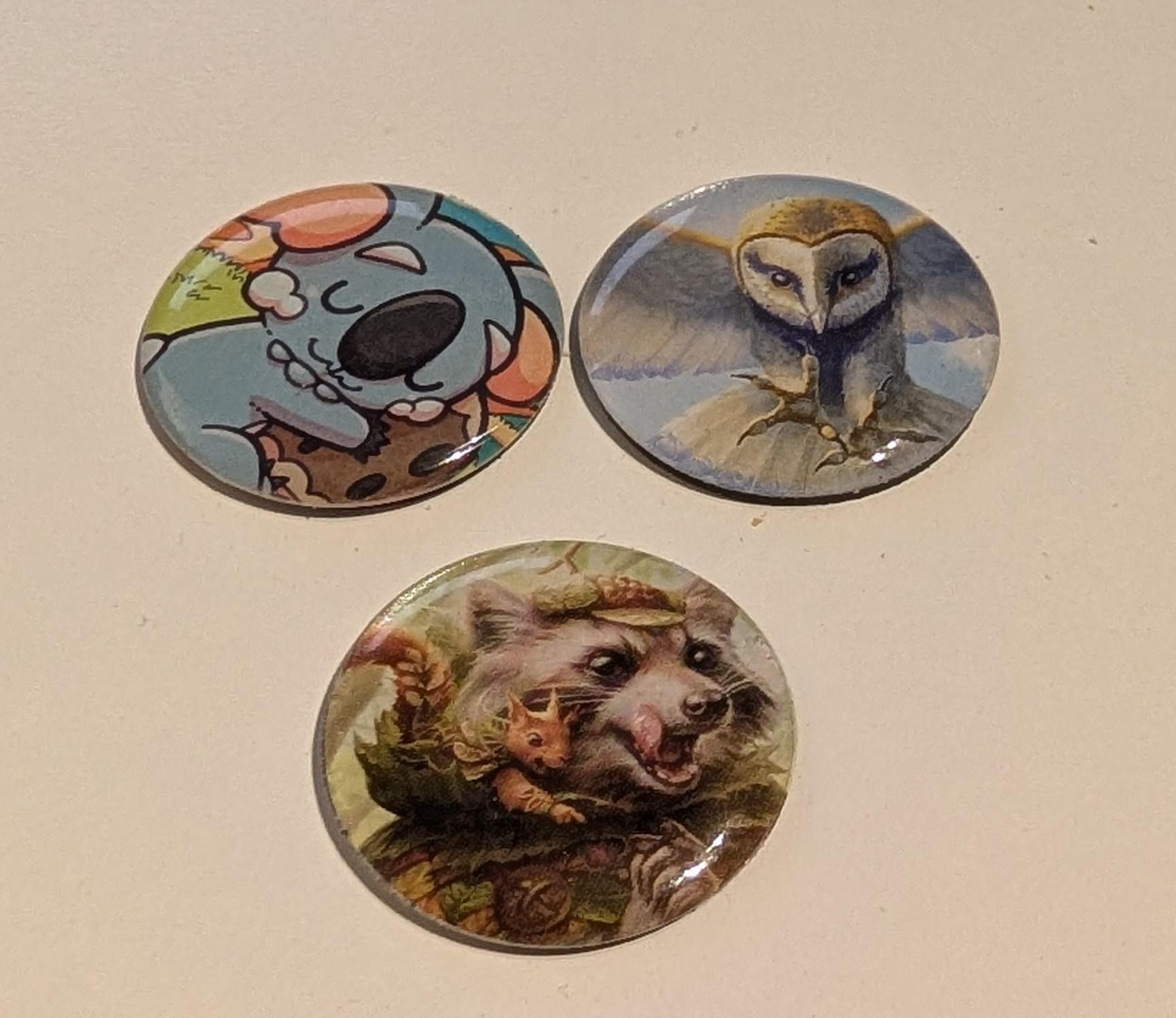Three round 1 inch tokens with illustrated baby koala, an owl and a raccoon art and a bit of shine from acrylic clear tops
