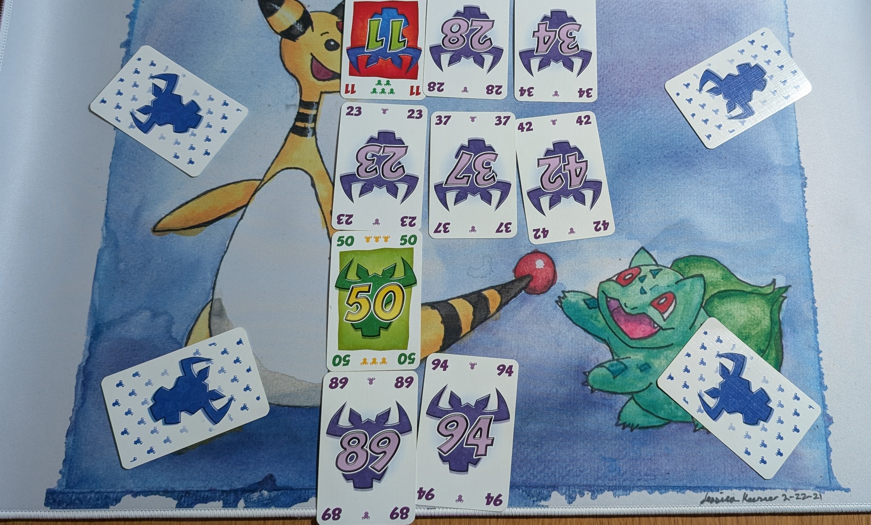 A game of 6 Nimmt on-going with four rows of 1 to 3 cards in each. Four cards have been played face down in each corner by different players.