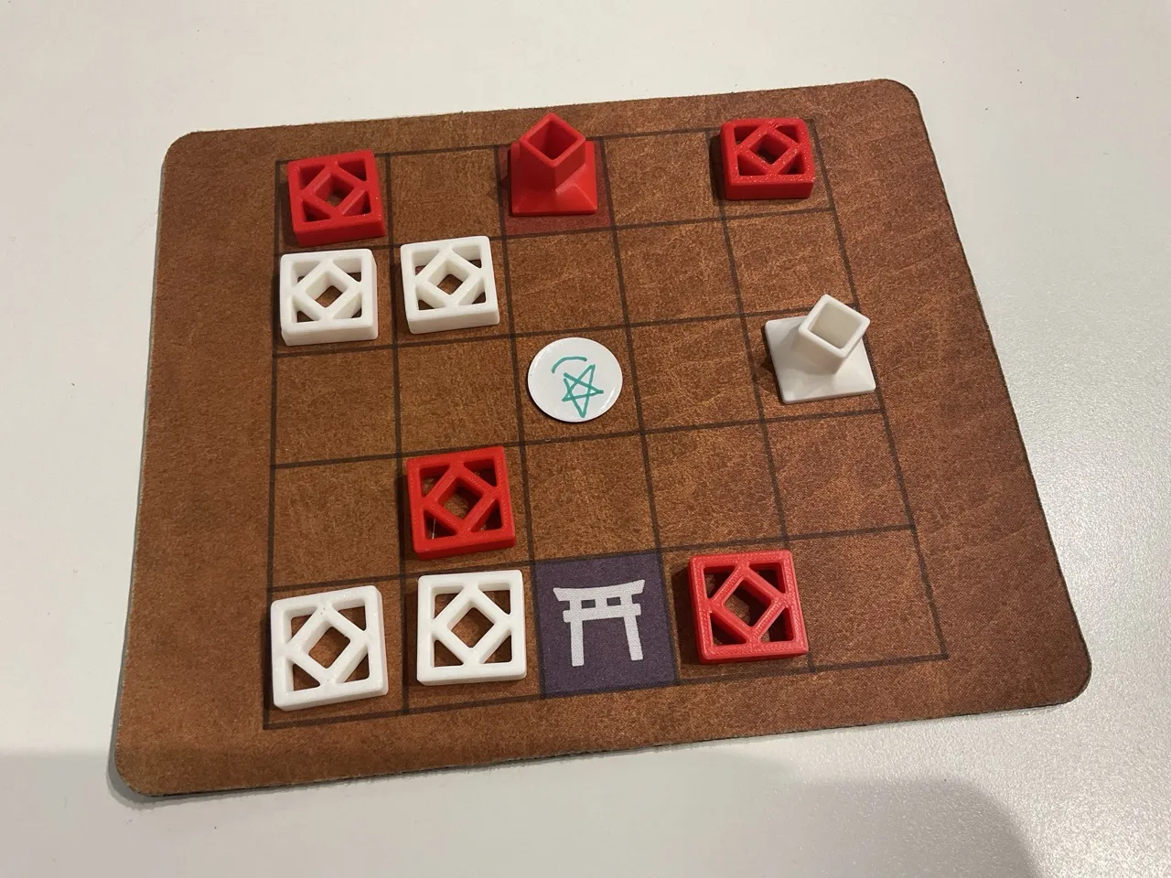 A game of King's Valley between red and white tiles. In the center square of a 5 by 5 grid, there's a white circle token with a handdrawn star on it.