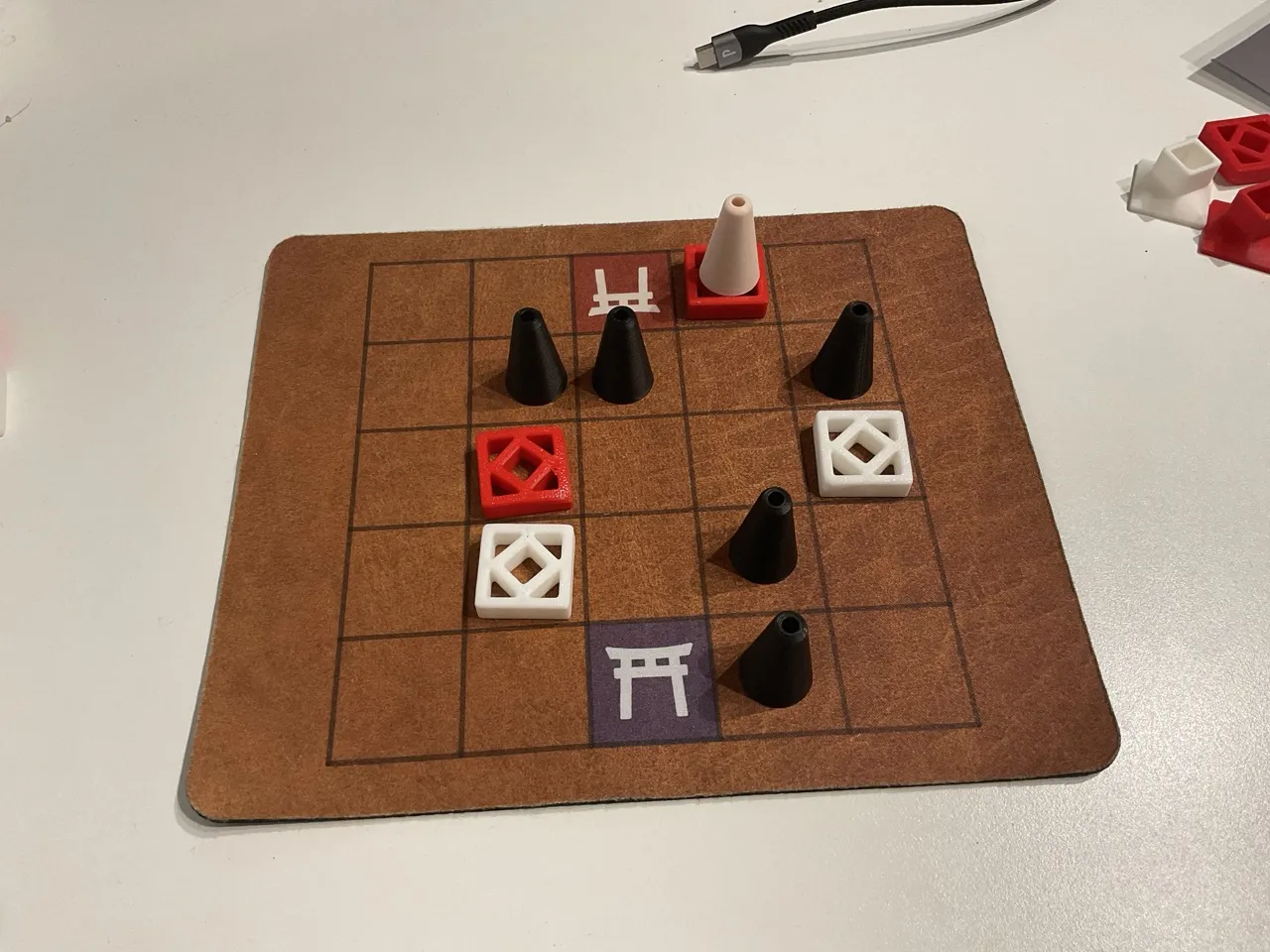 A game of Surikata with five black cones as mounds, two white tiles spread across the board and two red tiles. One of the red tiles has a beige cone representing a meerkat on top of it.