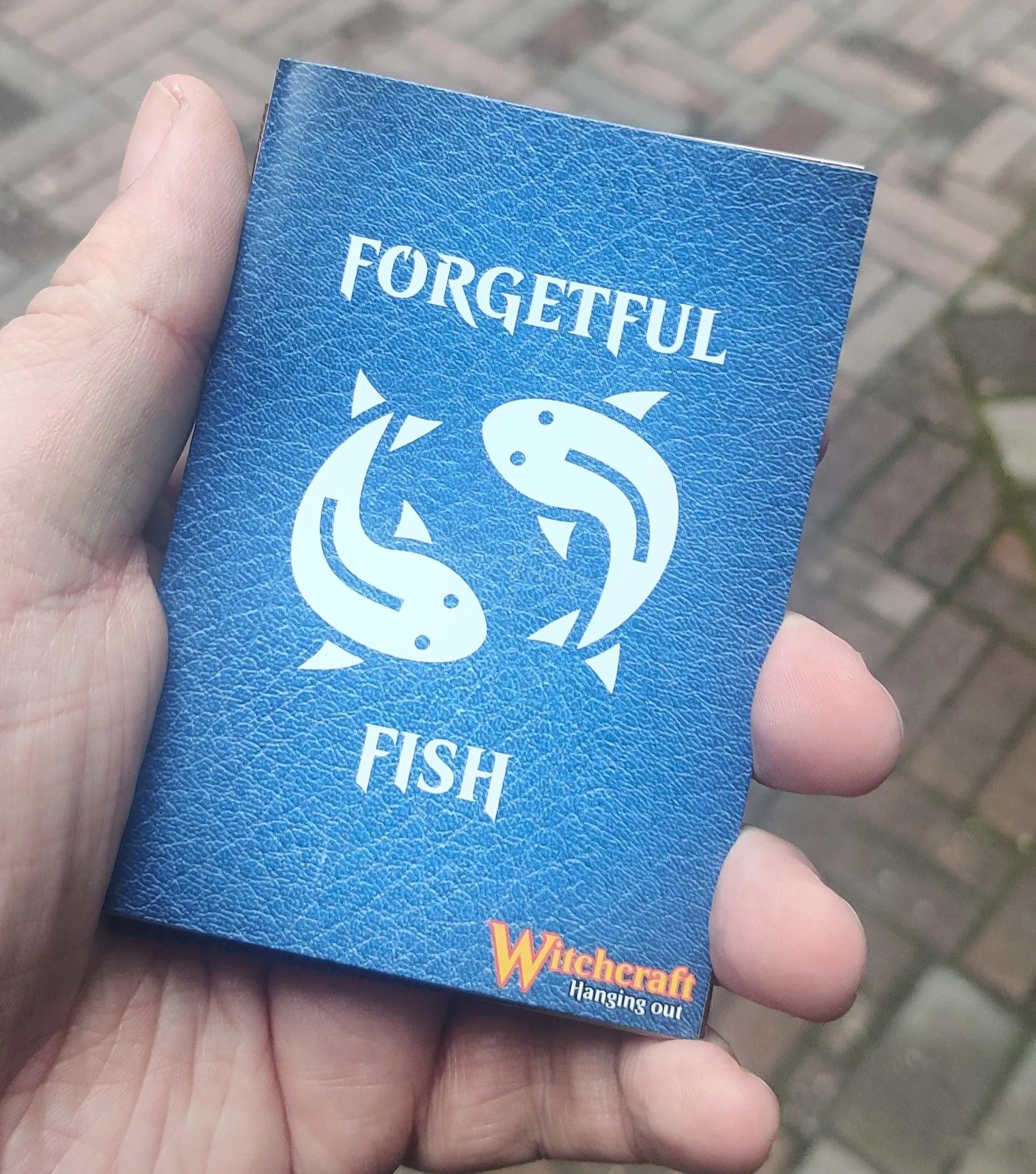An A7 size booklet with title Forgetful Fish and two circling white fish as a logo on top of a blue leather texture cover.