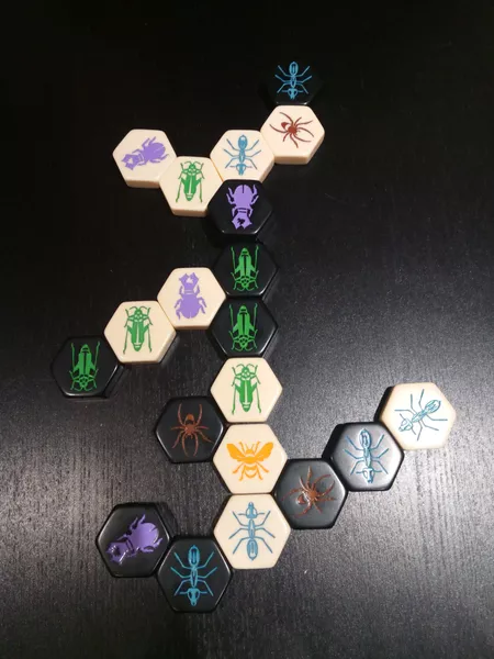 A late game position of Hive with a main column that branches out to different sized and shaped branches of tiles.