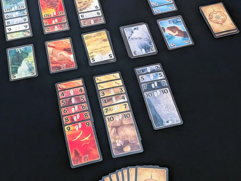 Lost Cities mid game. The cards are beautiful, richly coloured with beautiful art and they are played in five columns on two sides of a discard row in the middle.