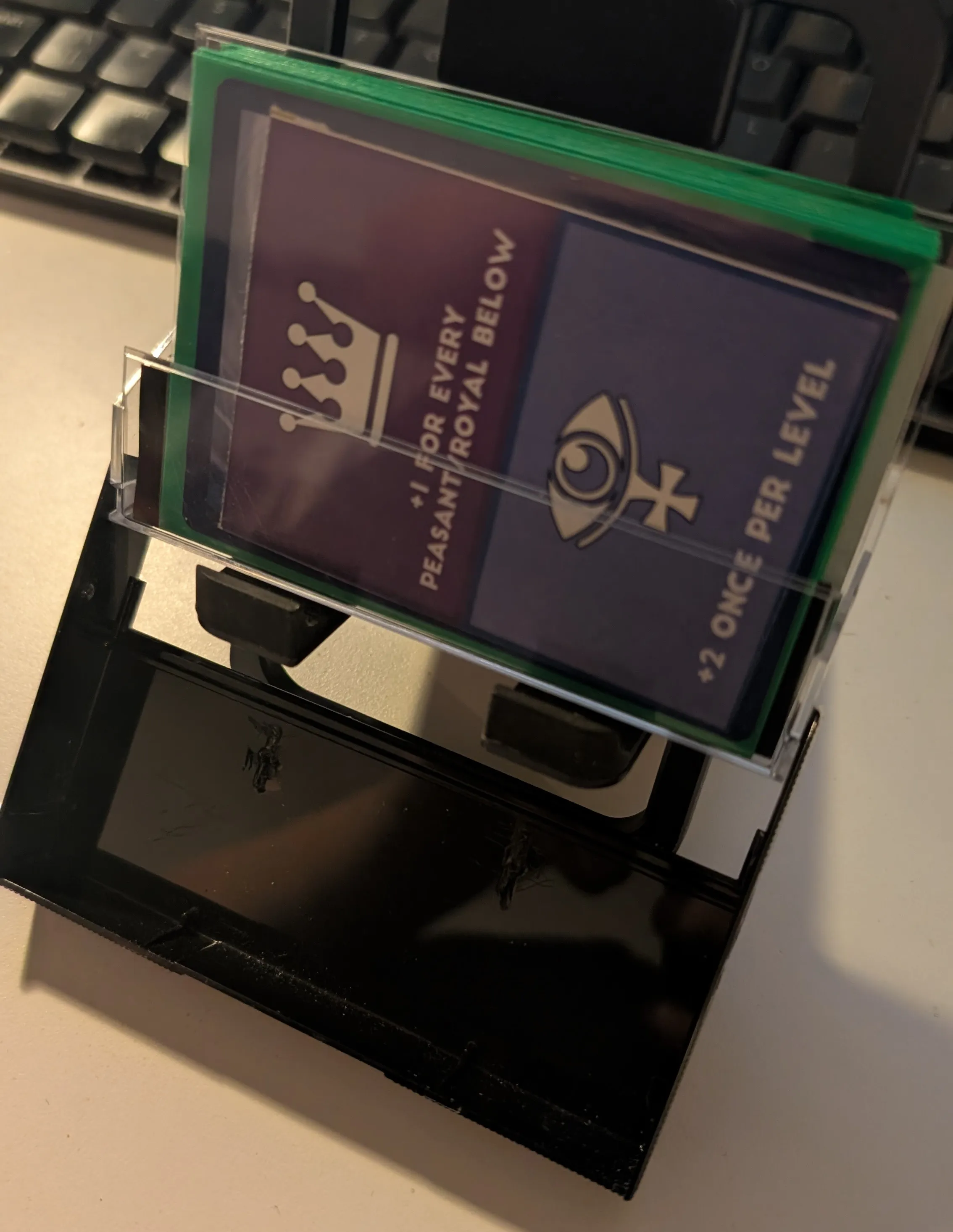 Open C cassette case with a small stack of cards in green sleeves inside. On top, a card with a Royal and Priest roles visible and a back of Pokemon TCG card is showing behind the printed card.