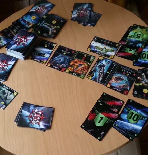 Star Realms being played on a small round table with cards all around the table, some face up, some face down.