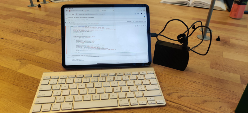 An iPad connected with a cable to a Raspberry Pi. A white wireless keyboard in front of it and a Jupyter notebook session on the screen.