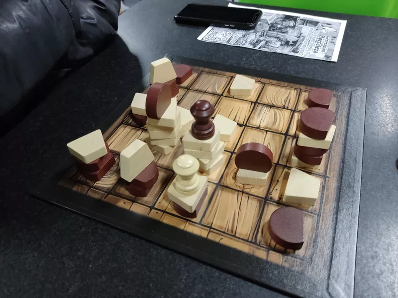 A late game position of Tak on a 5 by 5 board with dozens of brown and white pieces stacked in variously sized piles with plenty of empty squares.