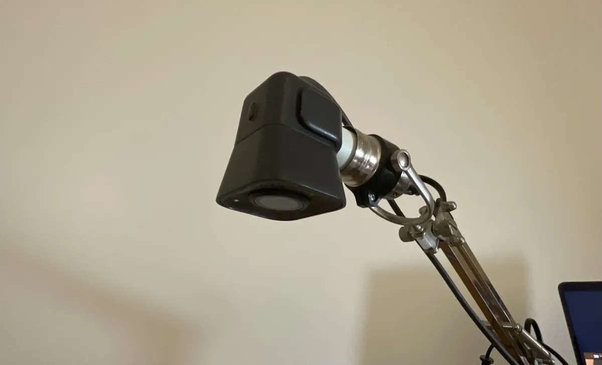 A webcam plugged into the light bulb socket of a metallic desk lamp stand.